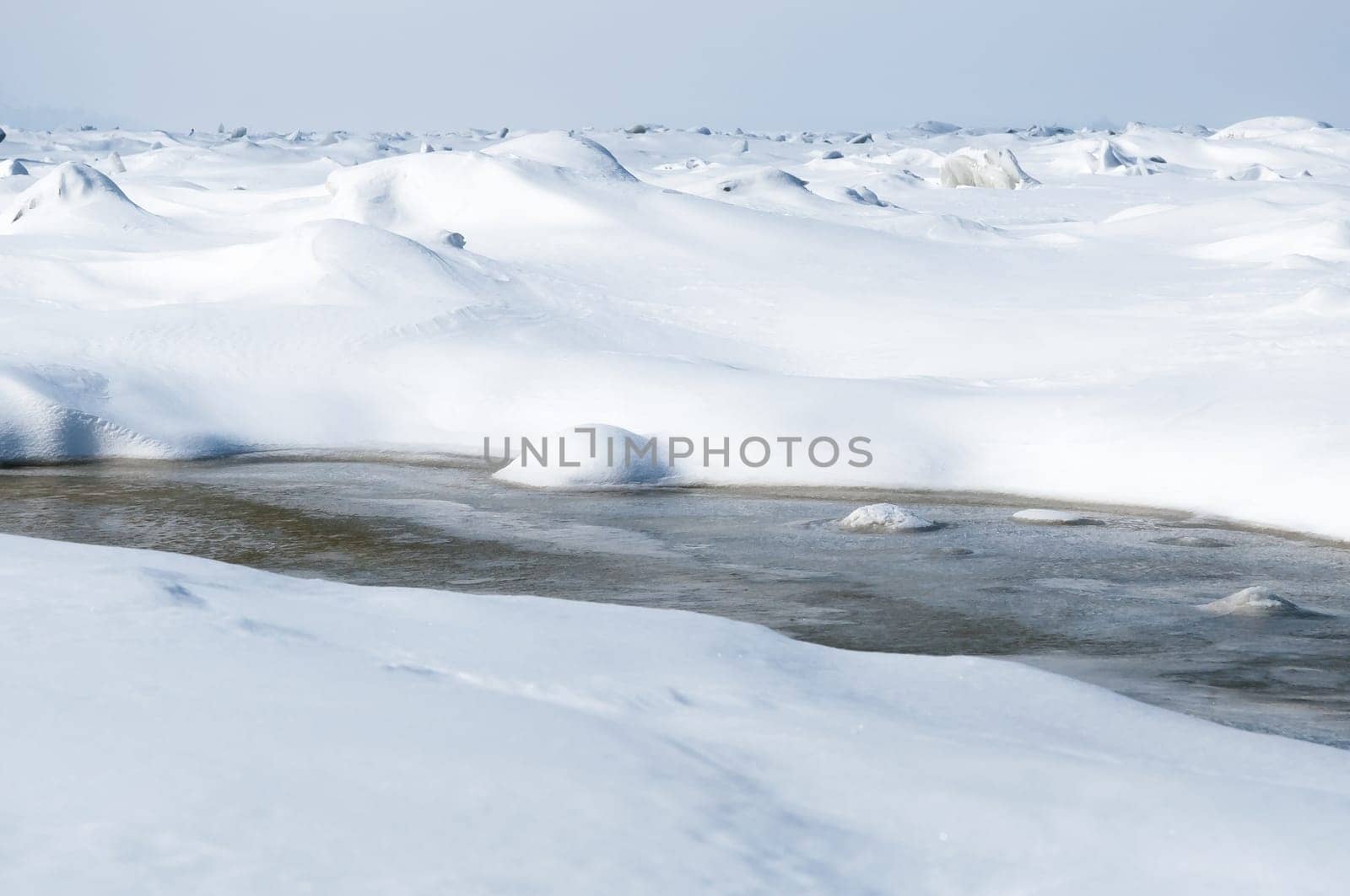 Stunning view of the frozen river covered with chunks of ice and white frosted snow. Snowy desert. The river breaks through the ice.