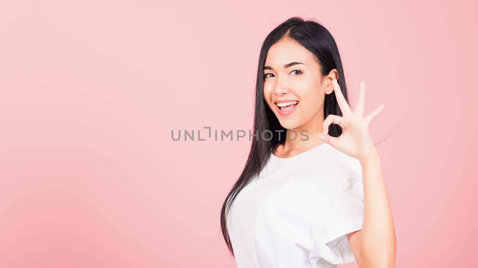 Portrait Asian beautiful young woman standing, She made finger OK symbol sign to agree side away looking at camera, studio shot isolated on pink background, Thai female agree hand sign copy space
