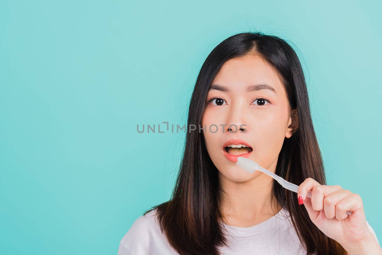 Asian beautiful young woman teen brushing teeth in the morning, portrait of happy Thai female confident smiling holding toothbrush, studio shot isolated on blue background, Dental health concept