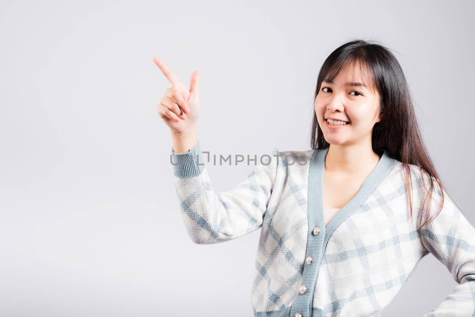 Smiling happy woman pointing finger out space, Portrait Asian beautiful young female point into empty looking to side away, studio shot isolated on white background with copy space