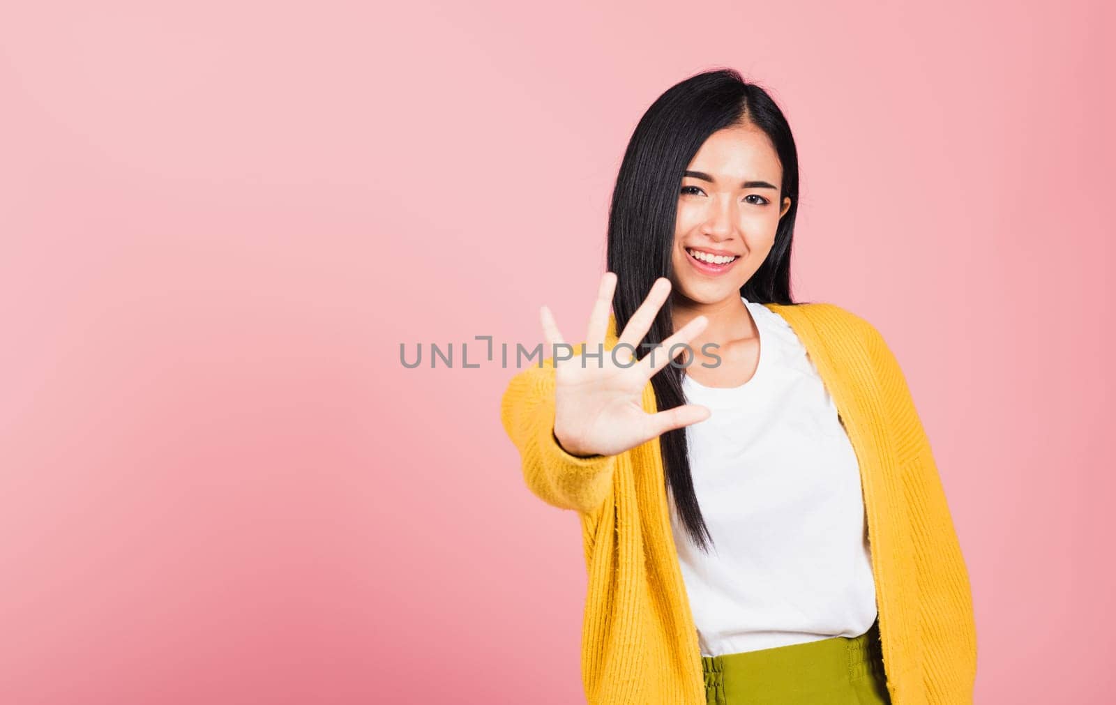 Asian portrait beautiful cute young woman teen smiling doing show stop sign gesture with palm of hand but happy face studio shot isolated on pink background, female doubt with copy space