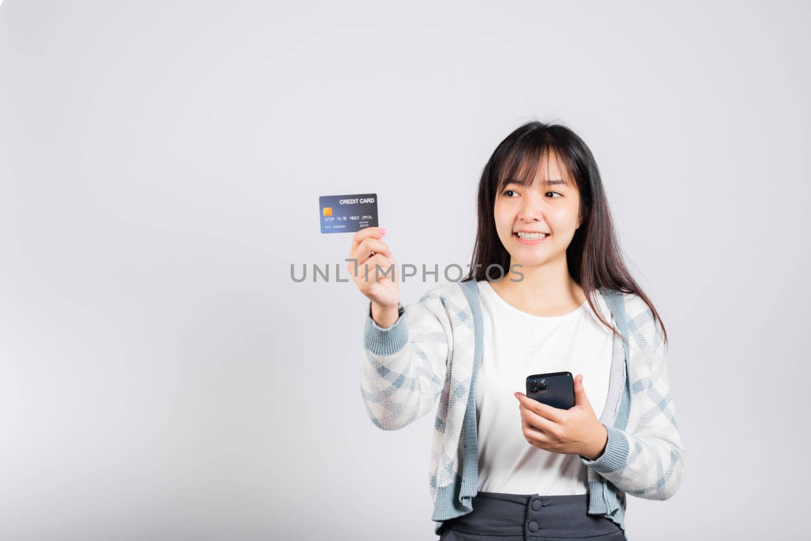 Woman excited smiling hold mobile phone and plastic debit credit bank card for payment studio shot isolated white background, happy young female using smartphone buy and pay online shopping