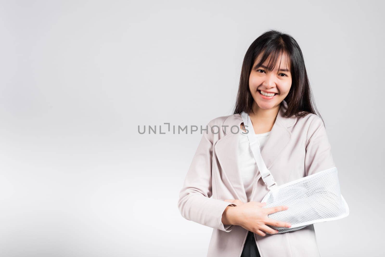 Arm broken. Business woman confident smiling broken arm after accident and wear arm splint for treatment, excited happy Asian female sling support hand studio isolated on white background, copy space