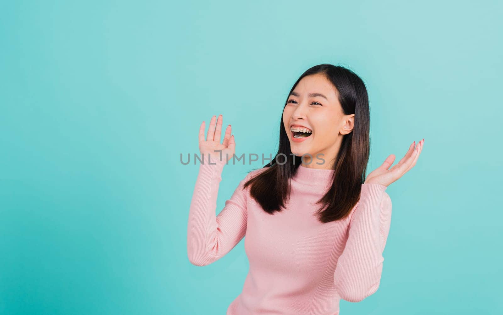 Happy young Asian beautiful woman smiling wear silicone orthodontic retainers on teeth surprised she is excited screaming and raise hand make gestures wow, studio shot isolated on blue background
