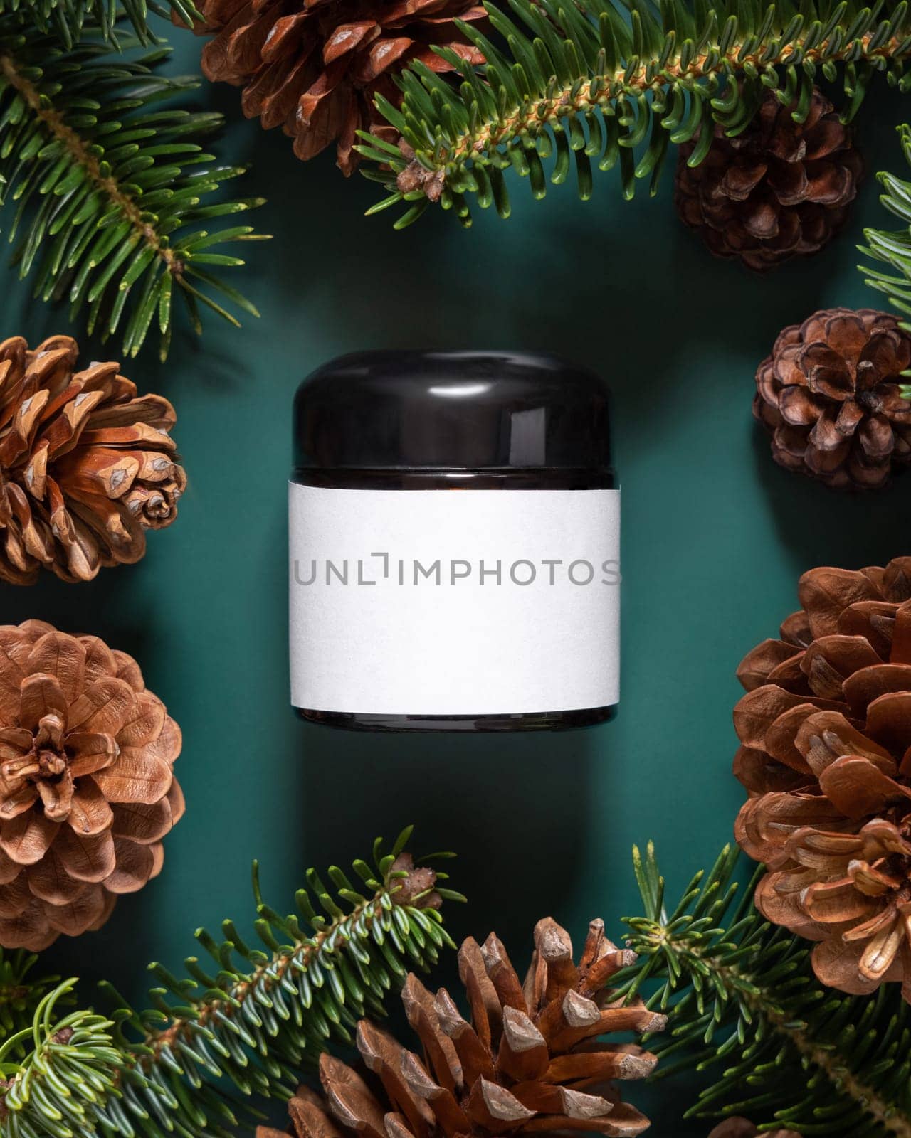 Brown glass jar near fir branches and pine cones on dark green top view. Brand packaging mockup. Skincare beauty product, cream or serum. Healthcare natural cosmetics concept