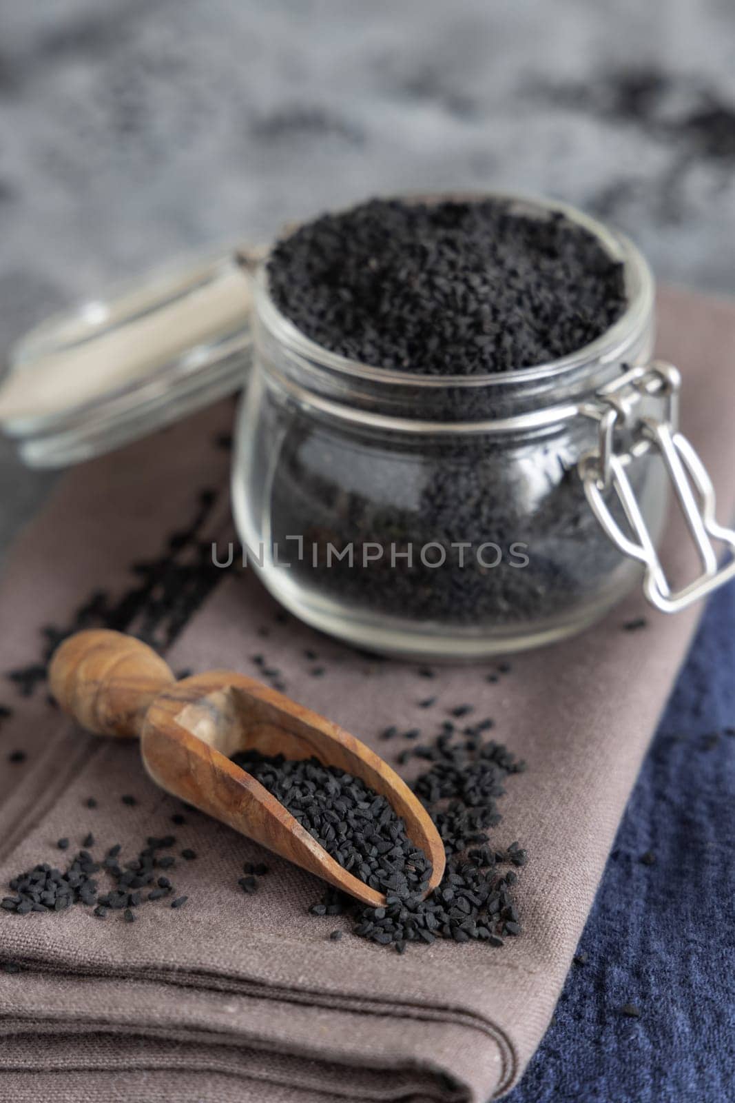 Indian spice Black cumin (nigella sativa or kalonji) seeds glass jar with a wooden scoop, close up. Traditional asian medicine, healthy and vegetarian food concept