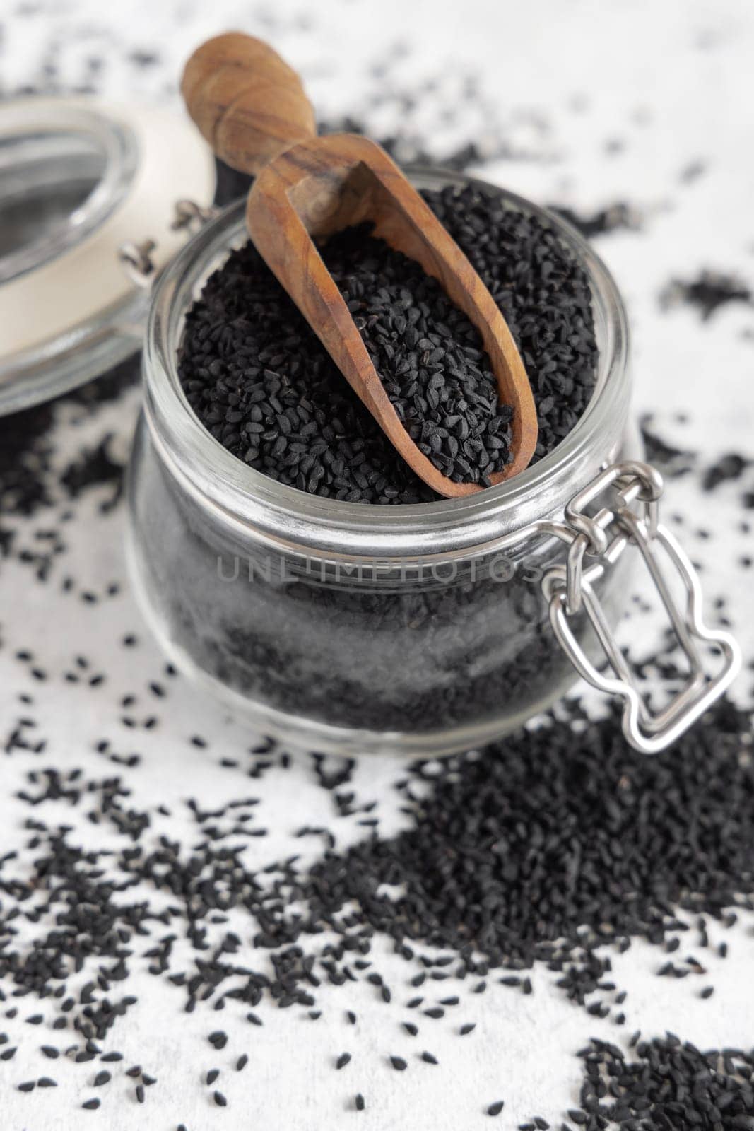 Indian spice Black cumin (nigella sativa or kalonji) seeds glass jar with a wooden scoop, close up. Traditional asian medicine, healthy and vegetarian food concept