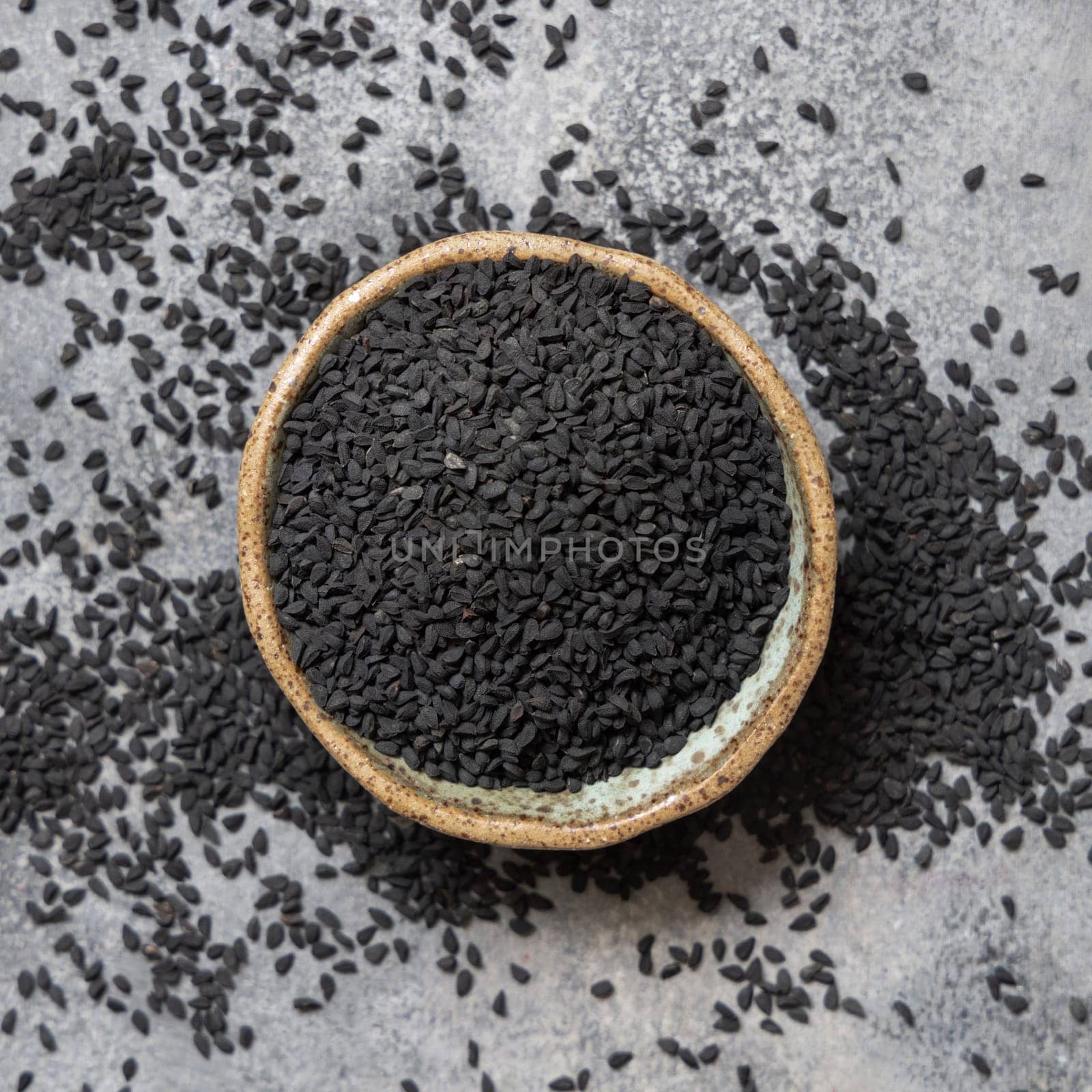 Indian spice Black cumin (nigella sativa or kalonji) seeds in bowl on grey table top view. Traditional medicine, healthy and vegetarian food concept.