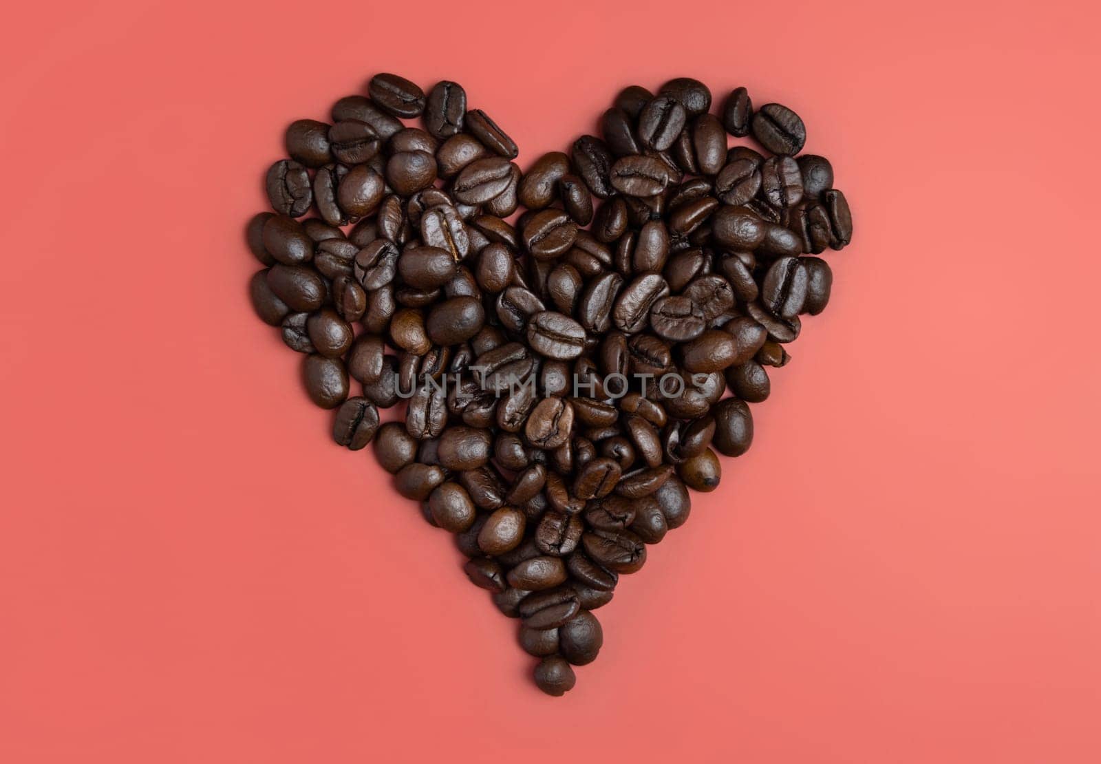 Heart made of Roasted Coffee beans top view on pink background. Represent breakfast, love, energy, freshness or aroma