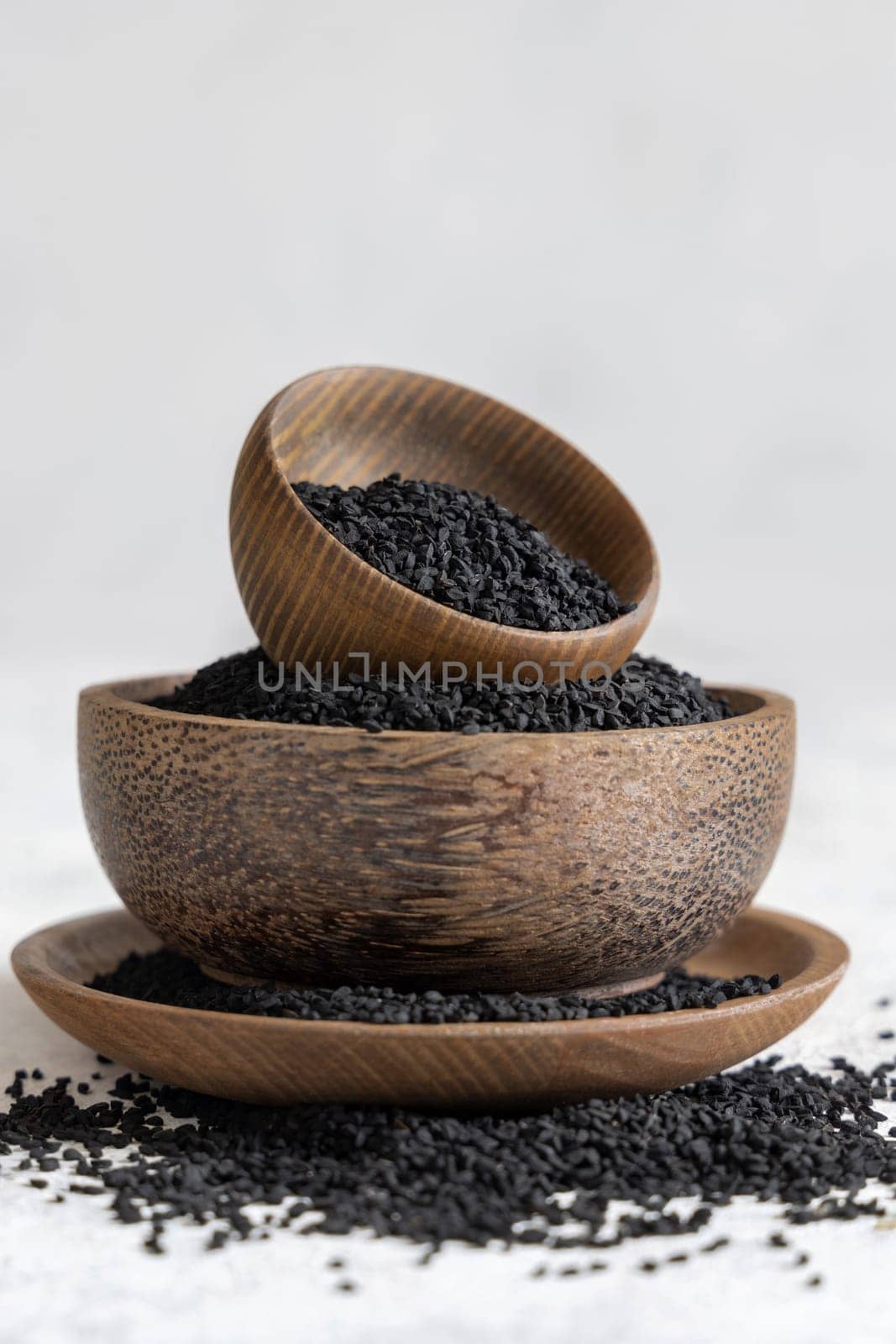 Indian spice Black cumin (nigella sativa or kalonji) seeds in wooden bowls on white table close up. Traditional medicine, healthy and vegetarian food concept.