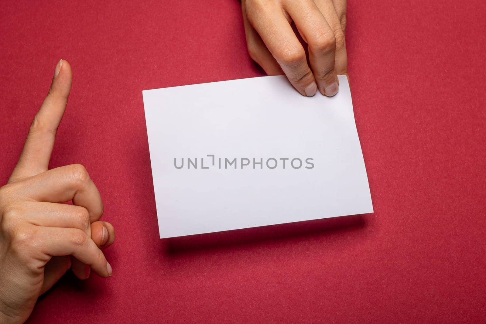 female hand holds a blank piece of paper with copy space in front of a dark red background cardboard with the hand making a warning gesture