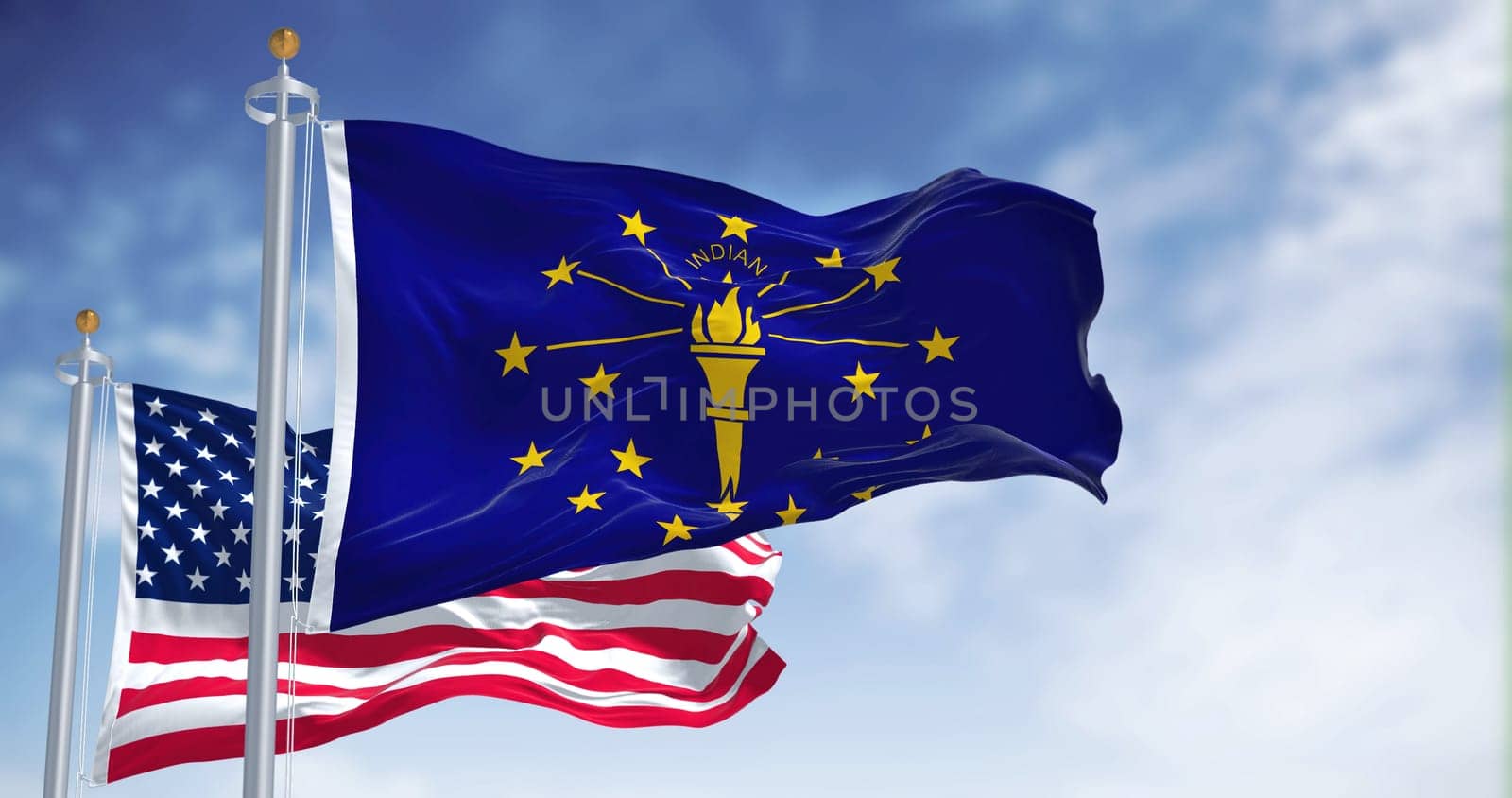 The Indiana state flag waving along with the national flag of the United States of America. In the background there is a clear sky. Indiana is a U.S. state in the Midwestern United States