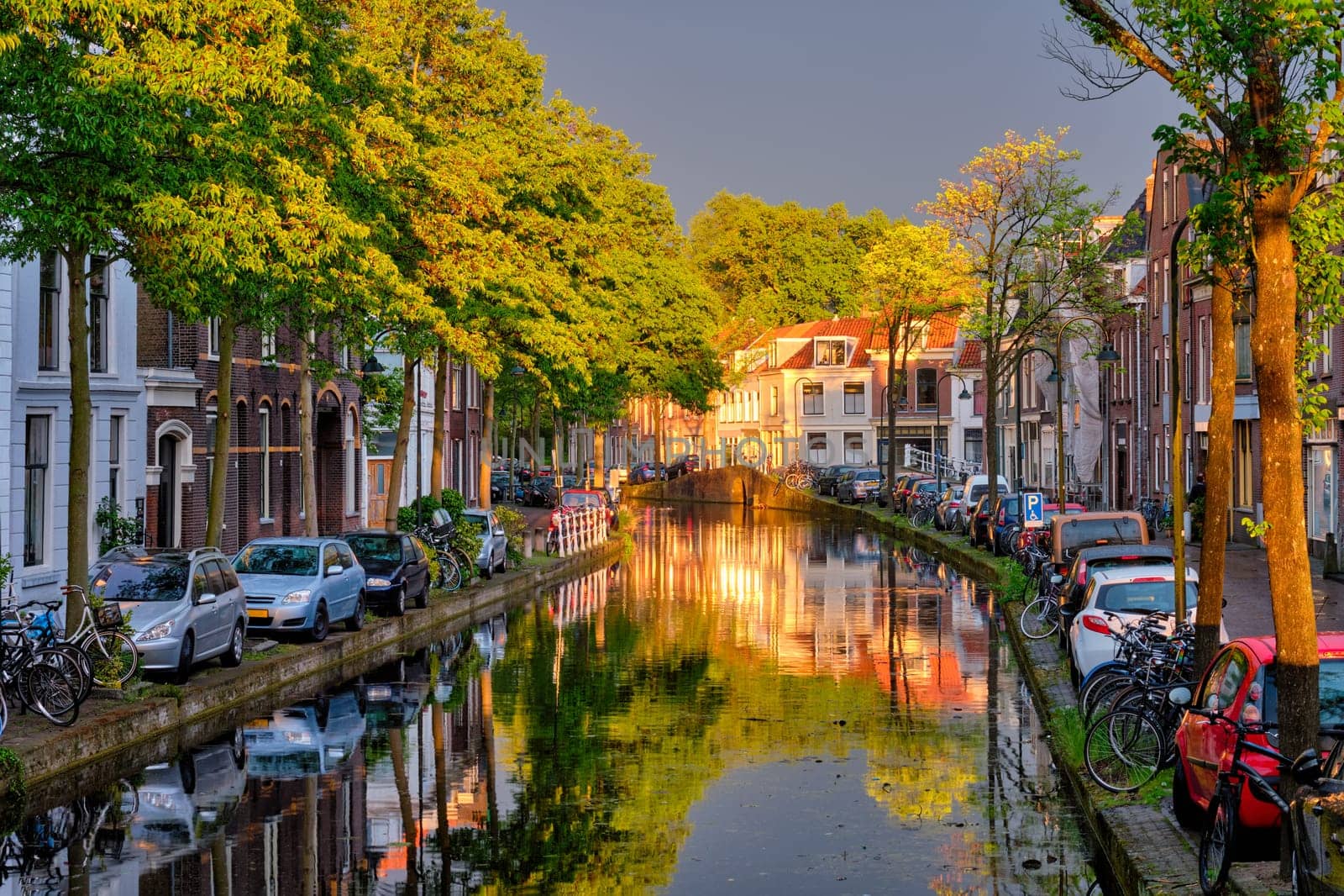 Delt canal with old houses and cars parked along on sunset. Delft, Netherlands