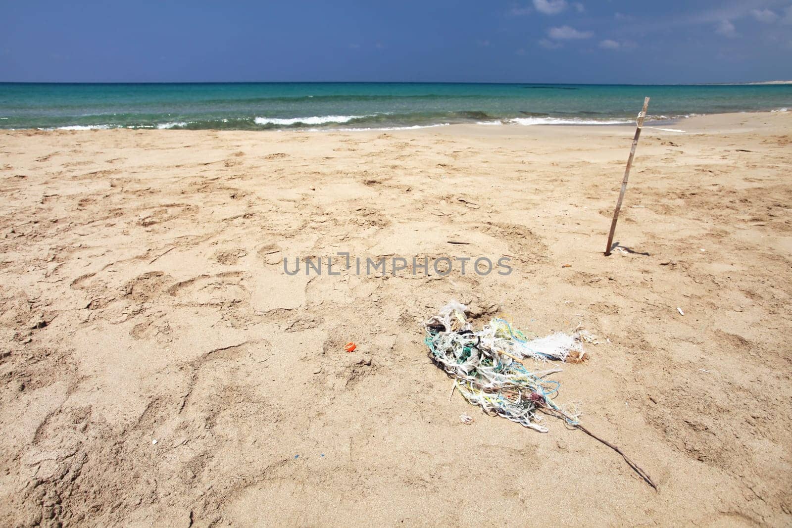 Beautiful empty beach, small pile of rubbish (tangled plastic ropes) on fine sand. Ocean littering concept. Karpass, Northern Cyprus