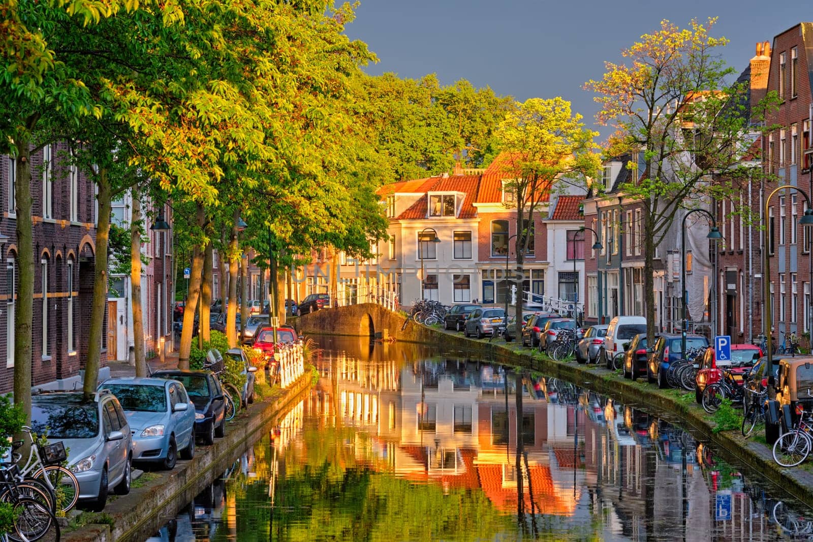 Delt canal with old houses and cars parked along on sunset. Delft, Netherlands
