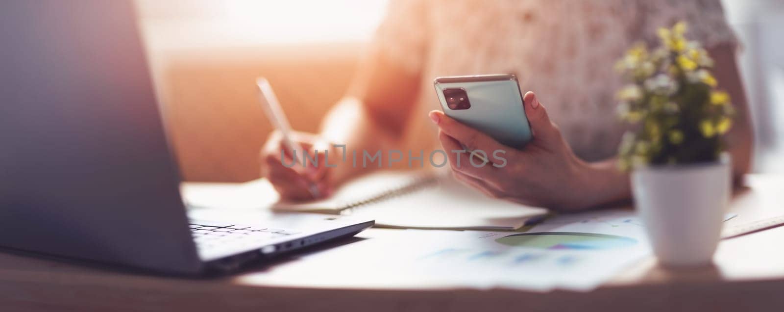 Woman writing in notebook and reading messages. Home office. Panoramic view.