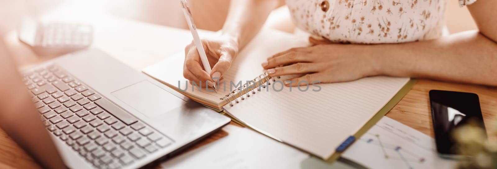 Woman writing in notebook at the office. Close-up panoramic view. Concept of the freelancer, studying at home and of doing business.