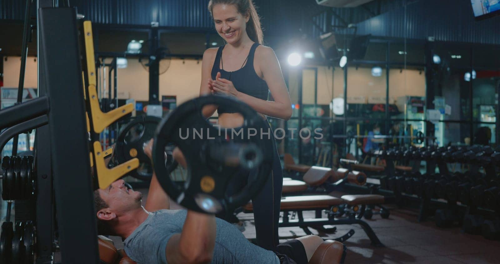 Personal trainer helping muscle man bench press weightlifting with barbell flexing muscles, woman training the man exercising power gymnastics, Sport fit workout bodybuilding concept