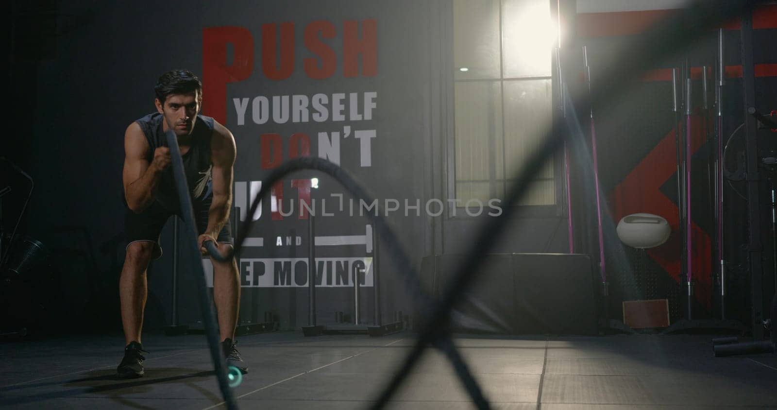 Muscular athletic Caucasian young man strong effort with battle rope waves doing exercise while working out in fitness gym, Cross fit training, People power sport health lifestyle concept