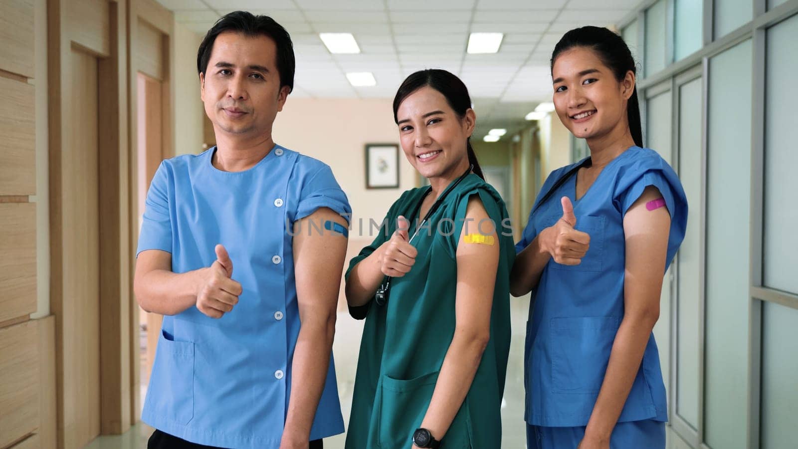 Medical personnel showing thumbs up and bandage with plaster on arm after getting Covid-19 vaccine, happy nurse woman and man standing at hospital, Covid-19 vaccination concept