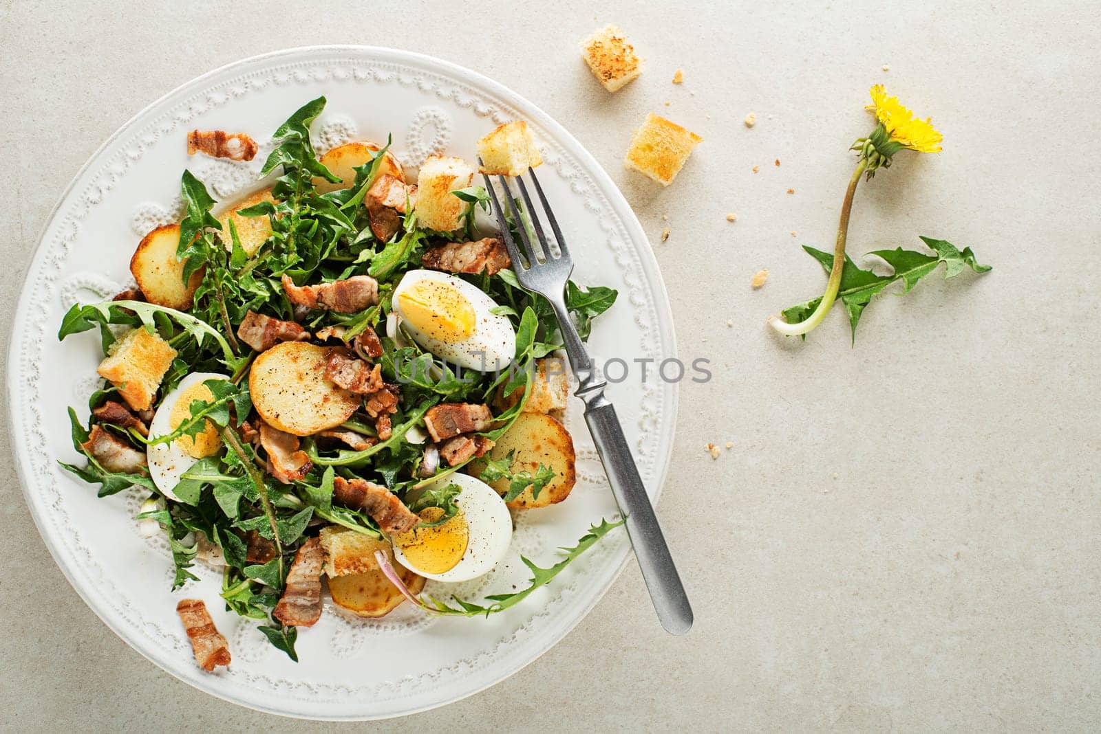 Dandelion salad with egg bacon potato and croutons on grey background