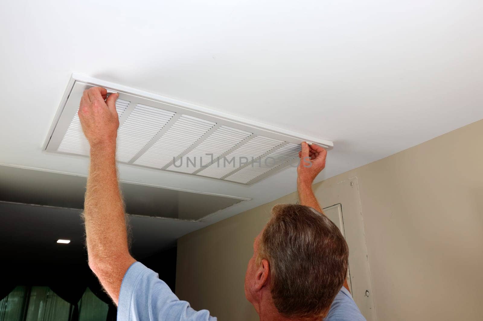 Adult human caucasian hands fingers holding air grid vent door fasteners ready to slide to open position to change the air filter. Ceiling air filter grid locks held by fingers ready to open the door