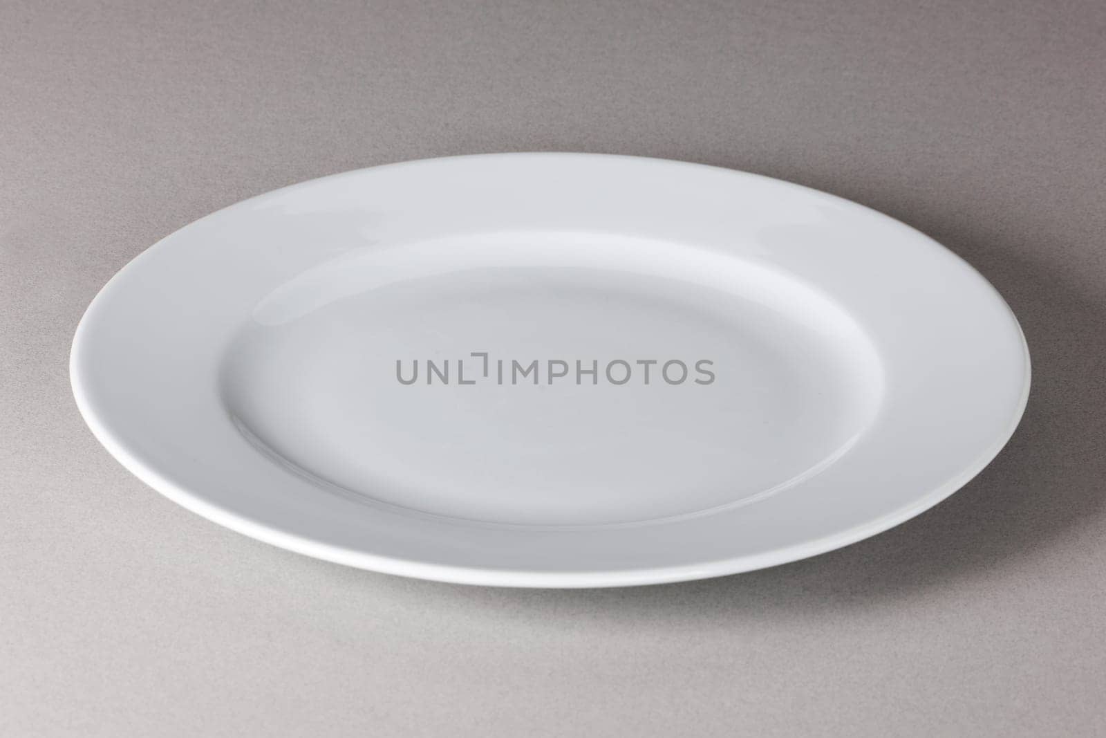 A raised view of a white dinner plate on neutral background with shadow