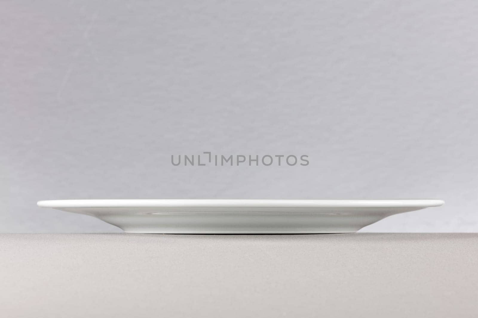A side view of a white dinner plate on neutral background