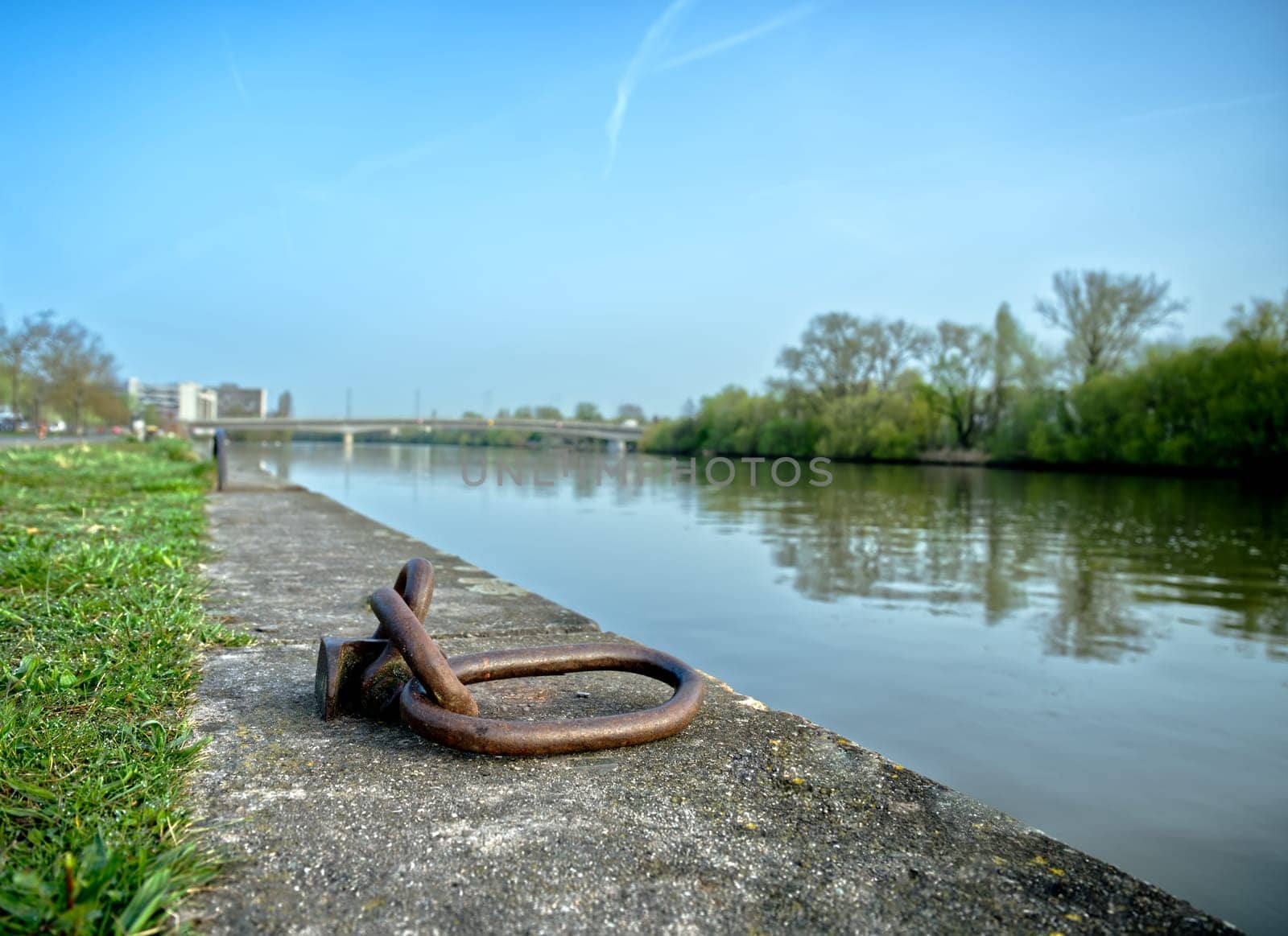 rusty metal loops for anchoring boats on the riverside at daytime, river and bridge in the background