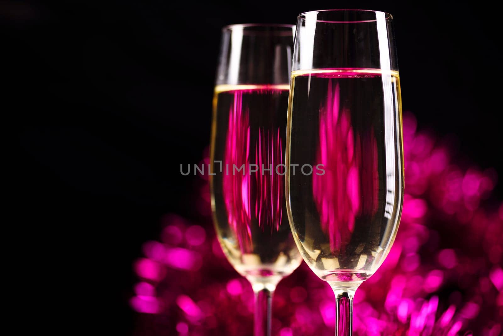 Two champagne glasses in front of purple sparkling background