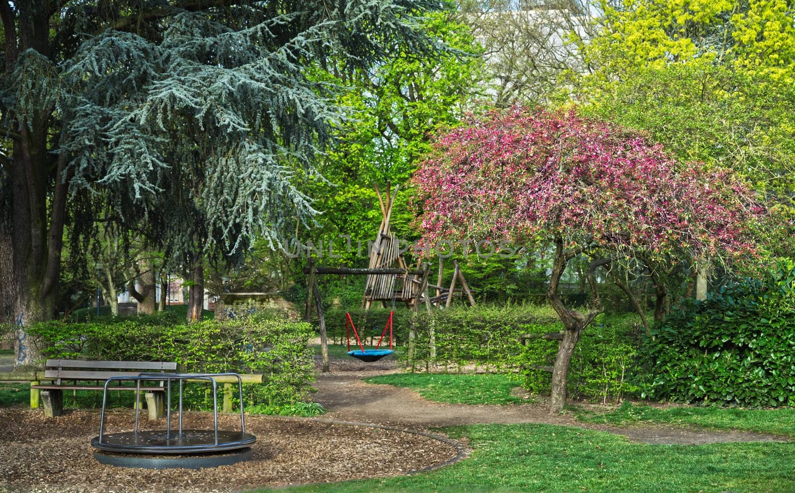 Idyllic playground with play equipment surrounded by various trees, blooming tree, swing and rotation equipment for children