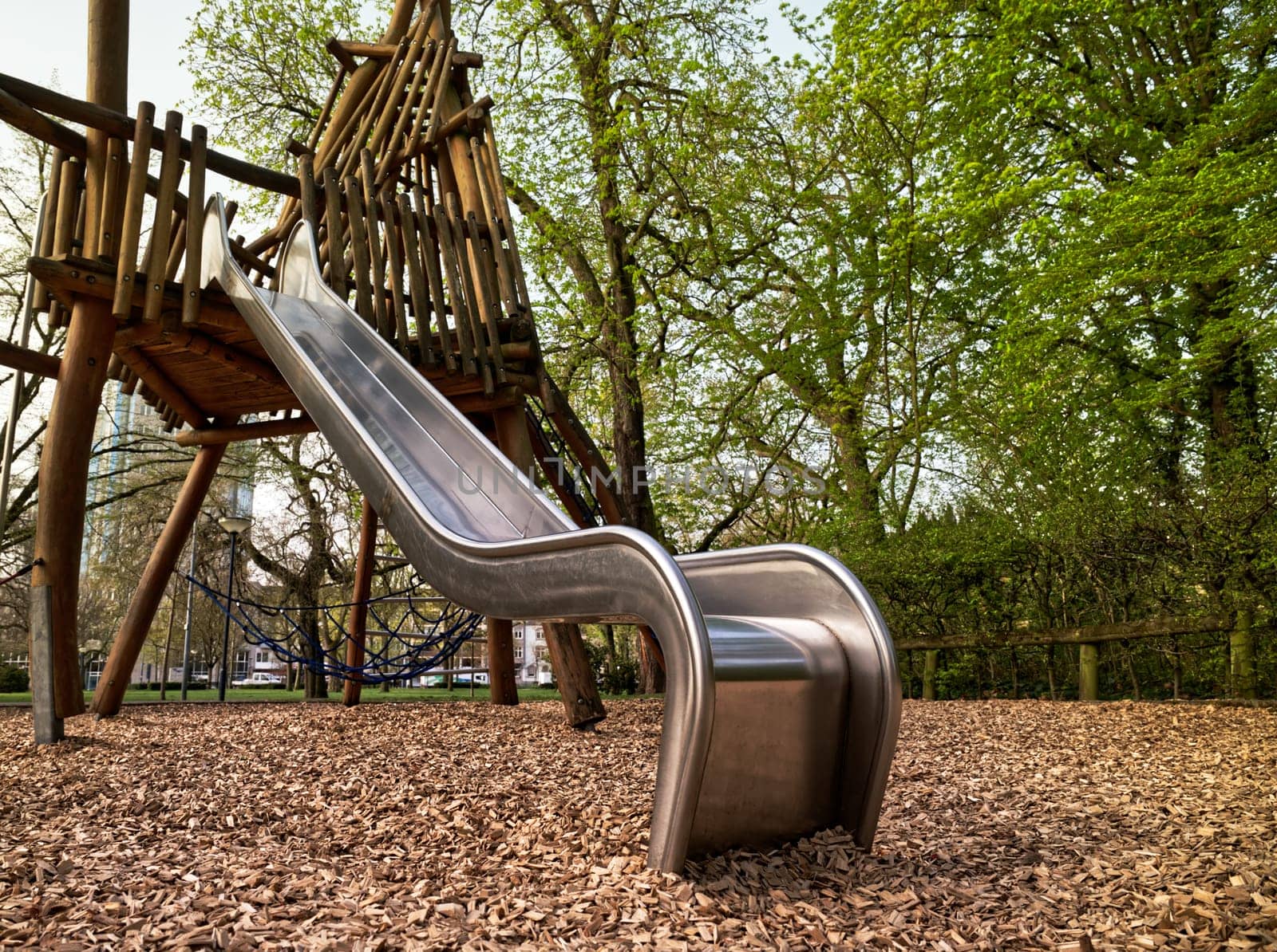 Playground with fokus on a silvery slide, wooden climbing frame in the background, worms-eye view