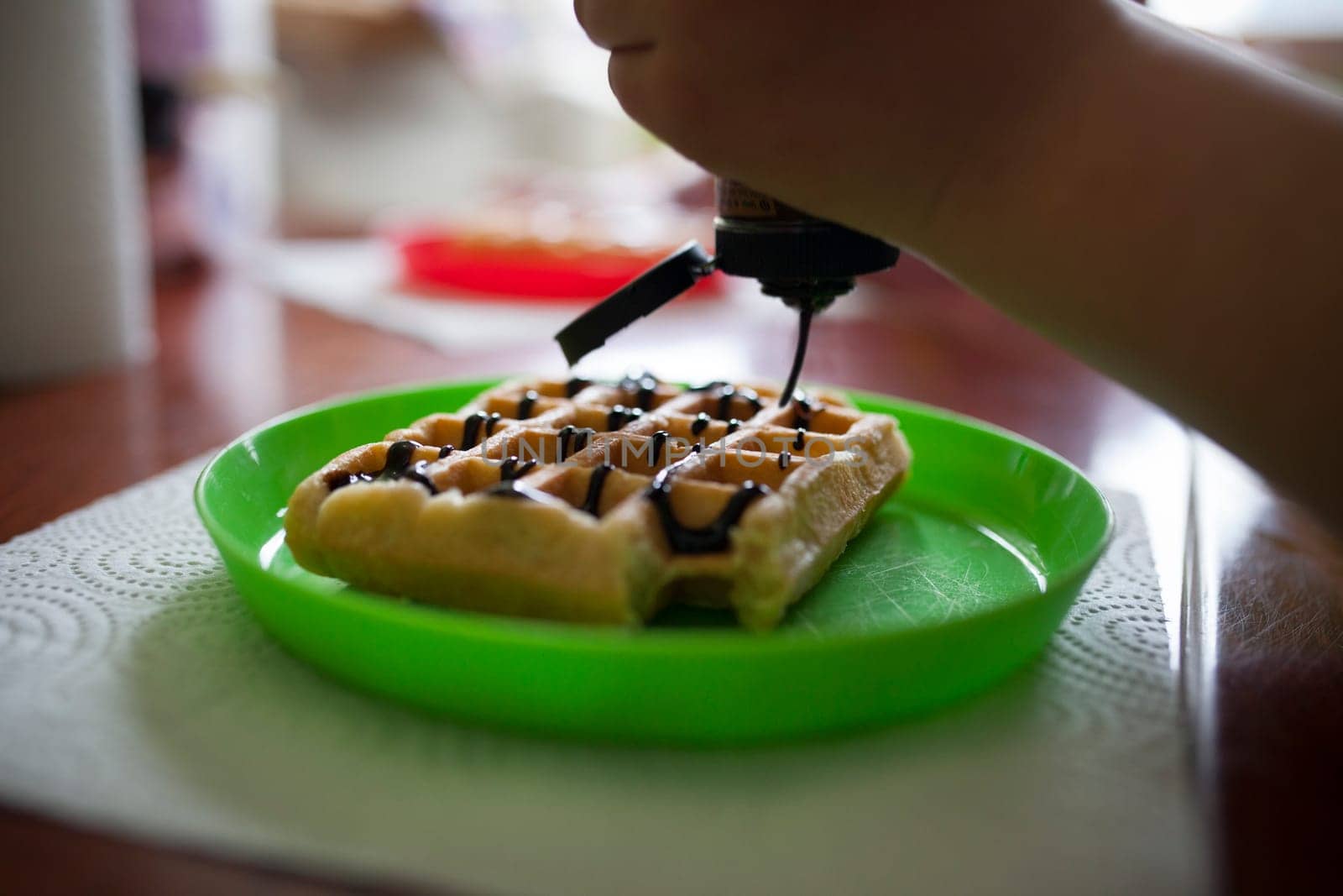 Child pouring chocolate syrup on a waffle. Closeup