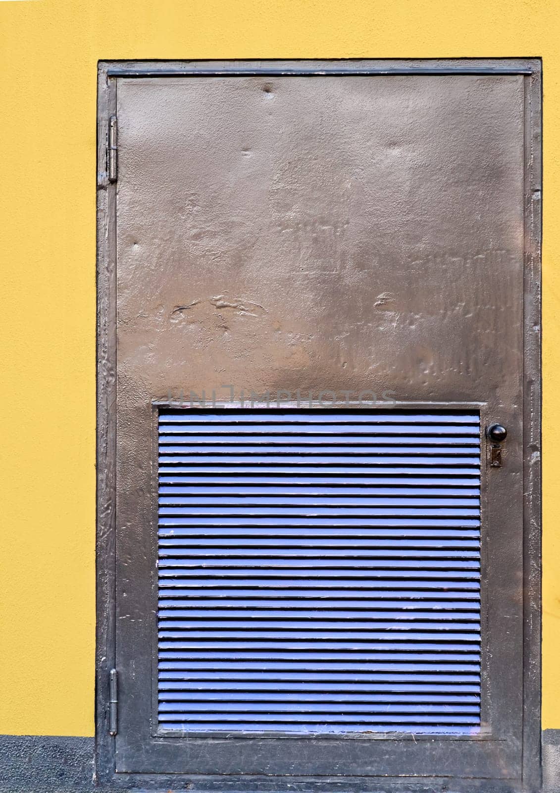 close up of a metal door of a transformer building, yellow painted walls, blue painted ventilation slits