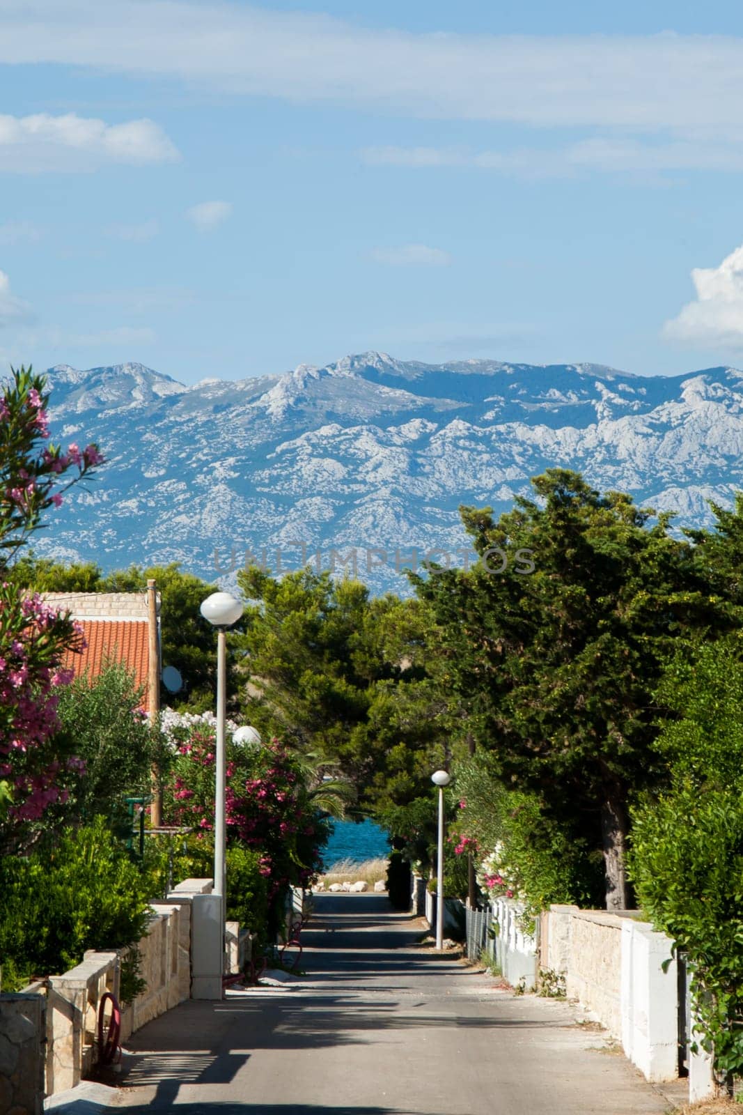 A small alley towards the sea in the apartment complex Lučica on the island of Vir, Croatia. View of the sea and the mountains.