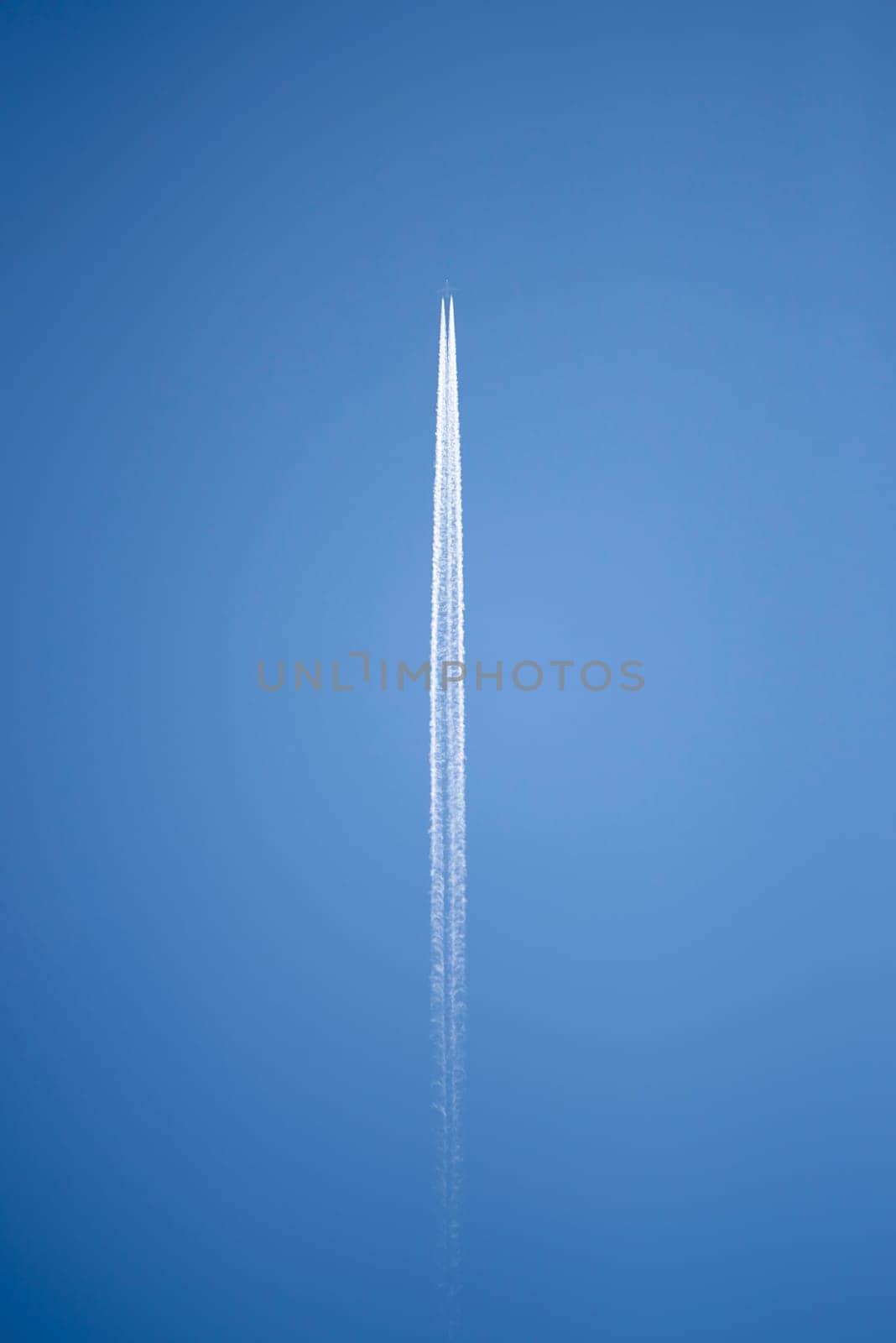 Aircraft flying high above leaving well-defined condensation trail behind it. Isolated against blue sky.