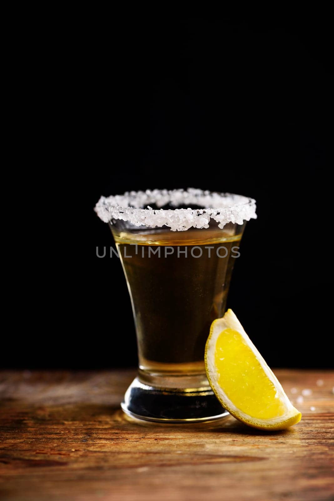 Tequila shot with salt on wooden table.