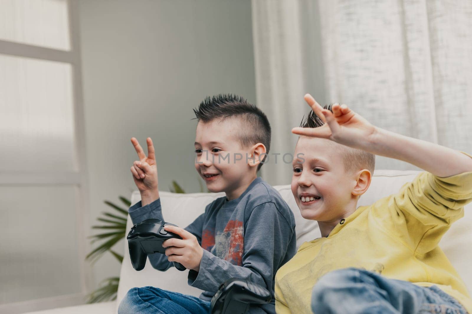 Two happy successful or triumphant young boys giving V-signs after winning while playing video games together on a sofa at home