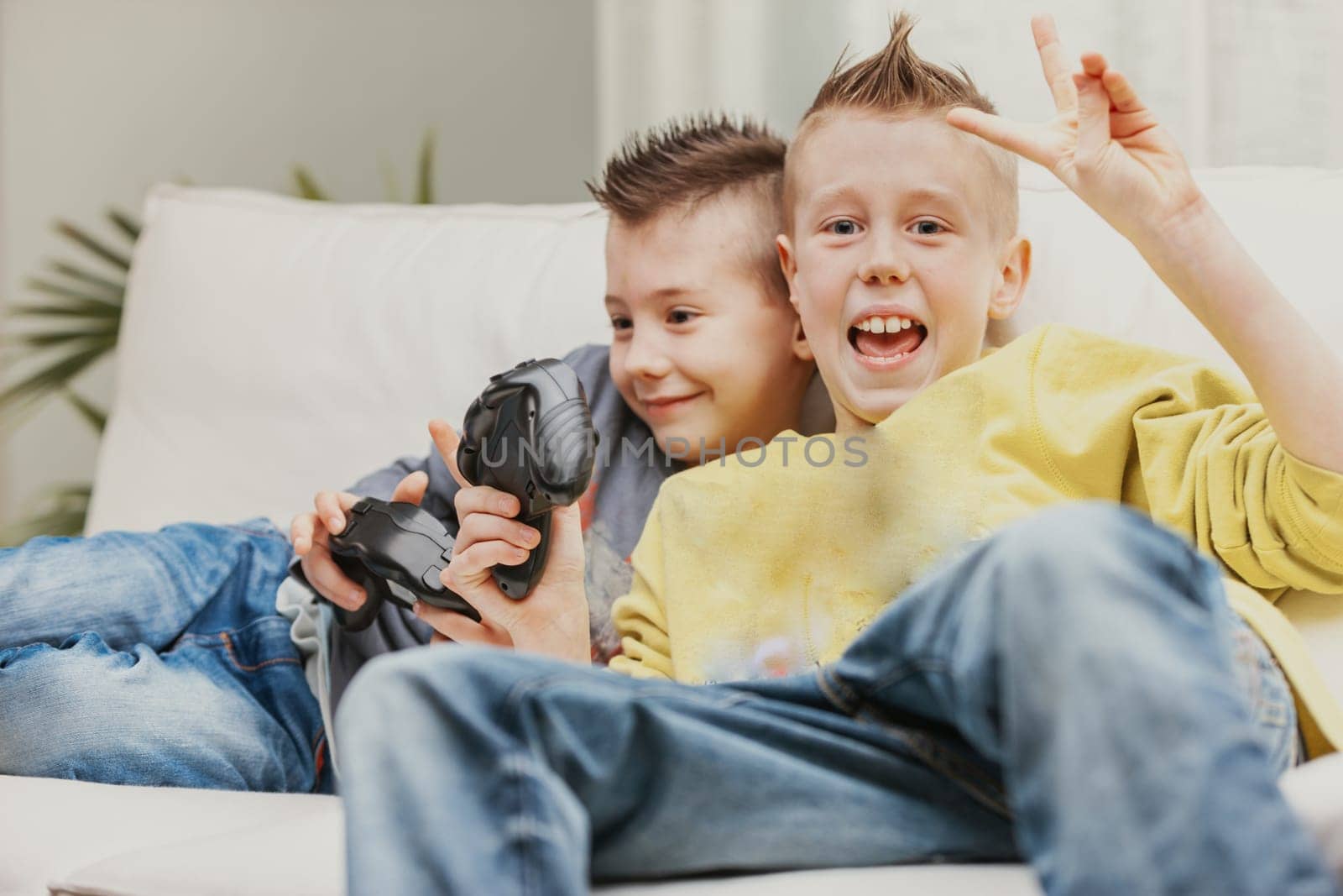 Happy young boy giving Victory sign with his fingers after beating his brother at a video game as they relax together on a sofa at home