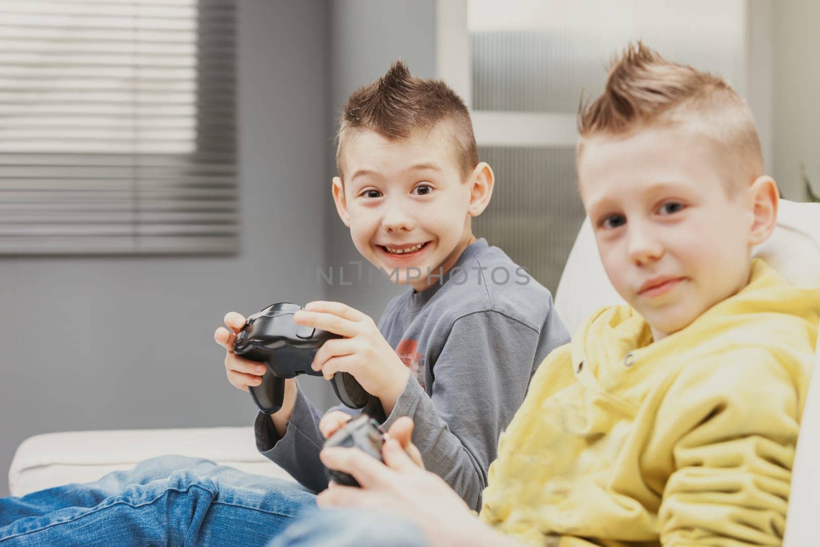 Mischievous charismatic young boy giving a toothy grin as he looks at the camera in excitement while playing video games with his brother