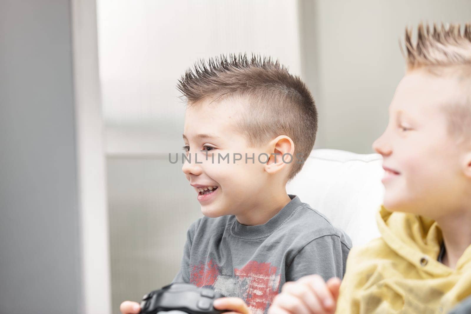 Candid high key portrait of a young boy playing video games with his brother smiling with glee as he watches the screen