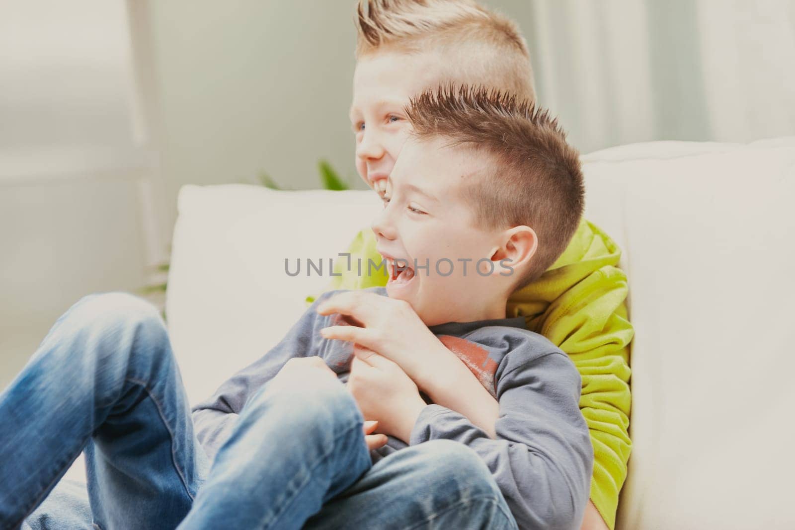 Two fun loving young brothers cuddling and laughing together on a sofa in a high key close up portrait