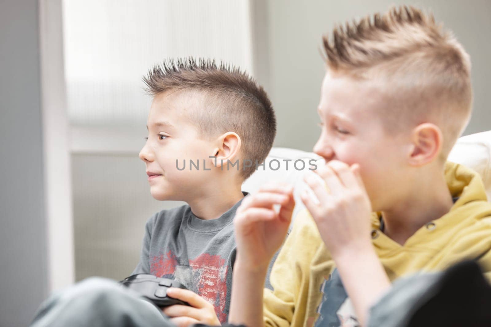 Young boy looking at his video game with disappointed expression as his brother bursts out laughing in delight as they enjoy a bit of competitive gaming