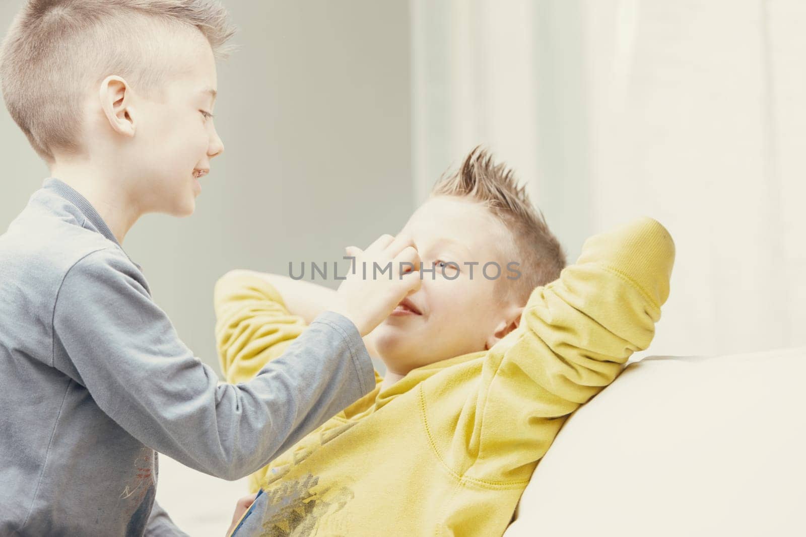 Two happy young brothers enjoying playing together indoors on a sofa in the living room in a close up high key portrait
