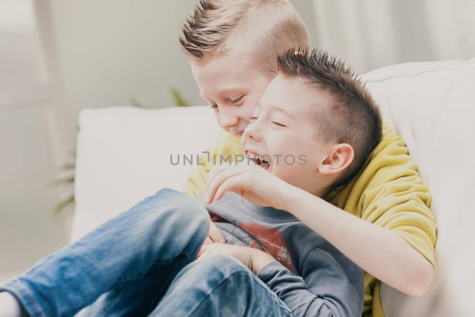 Two loving young brothers enjoying a rough and tumble on the sofa laughing happily as they tickle each other in a close embrace