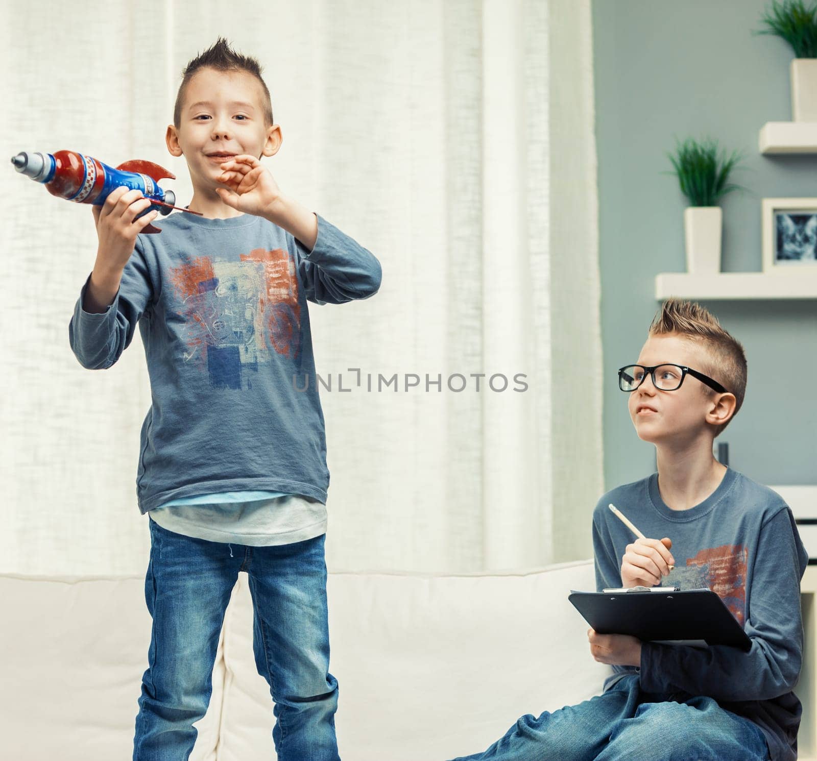 Two cute young boys with Mohican spiky hairstyles playing in a living room with a toy rocket with focus to a youngster standing grinning at the camera
