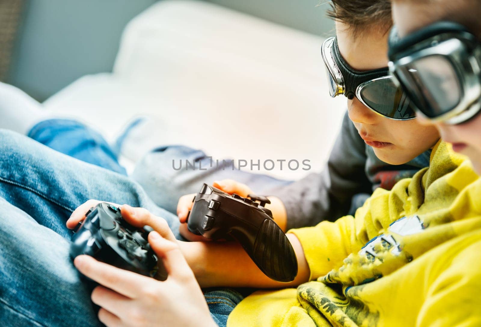 Young brothers wearing goggles huddling together playing video games on a sofa in a close up cropped view with focus to their hands and the controllers