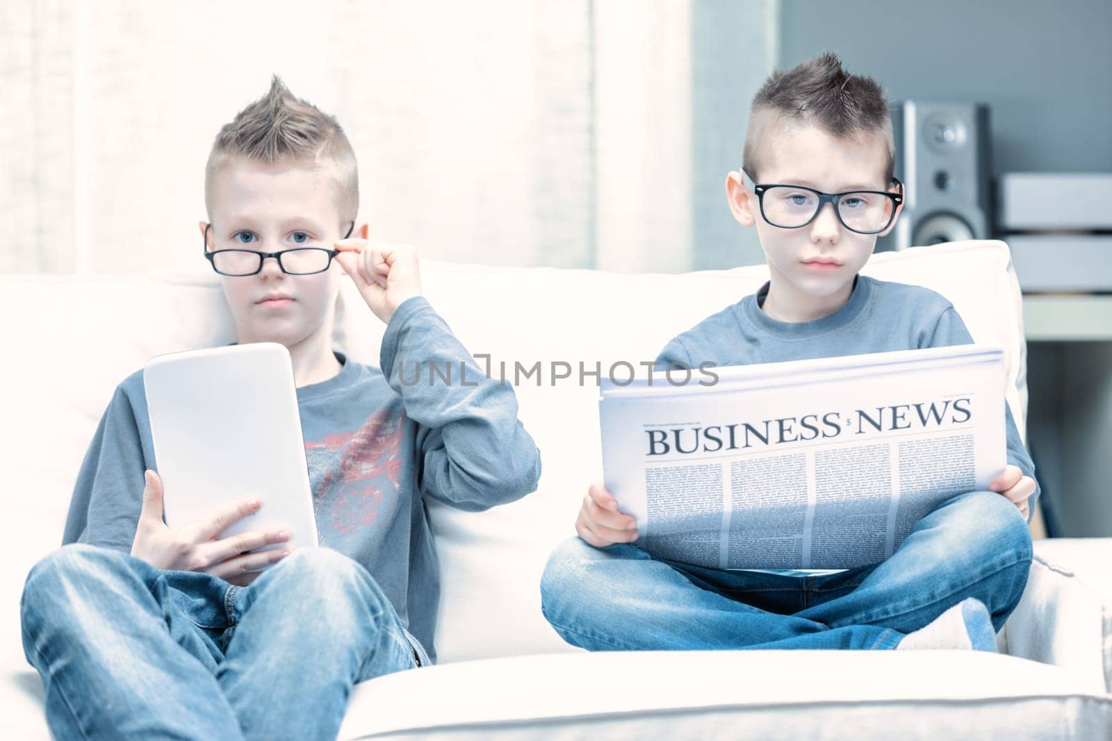 Spoof of two young boys wearing glasses posing as businessmen as they sit side by side on a sofa reading the Business Times and using a tablet