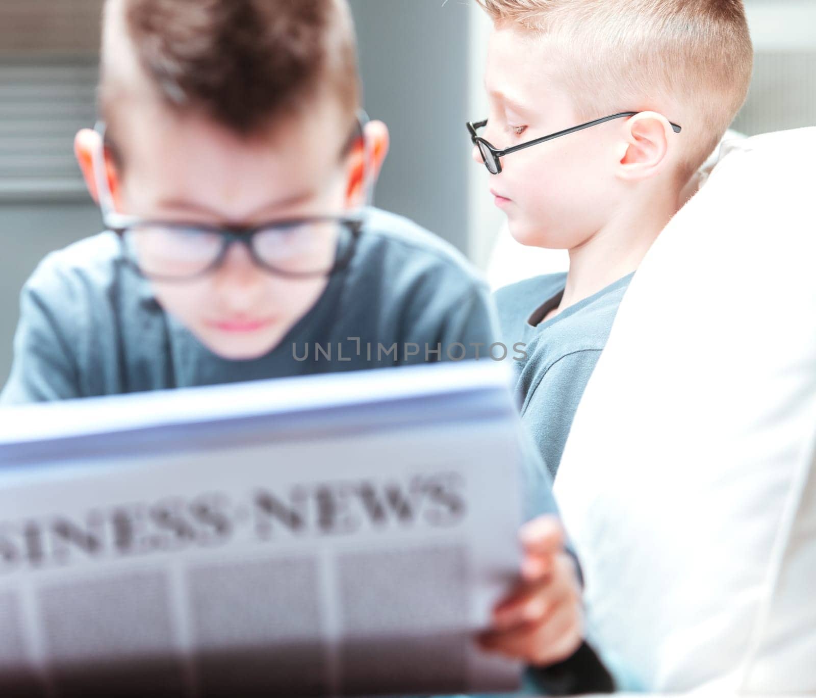 Two young brothers relaxing on a sofa reading with focus past a studious young fellow studying the Business News to his sibling beyond