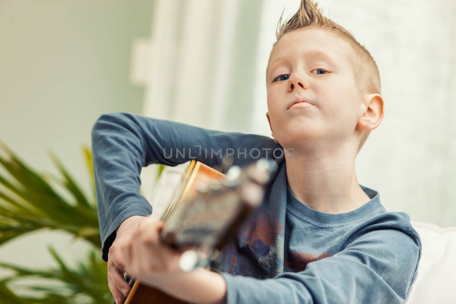 Young boy playing his guitar for the camera in a close up portrait conceptual of childhood hobbies and talent